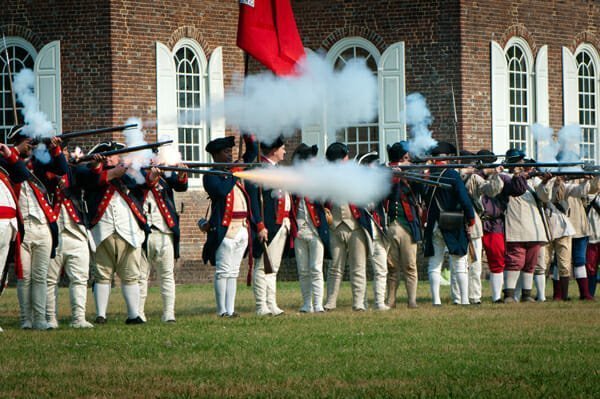 Colonial Williamsburg, USA - June 1, 2011: Renactment in Colonial Williamsburg, Virginia. A lineup of reenactors -dressed in Washington´s troops uniforms- shoot musket rifles.